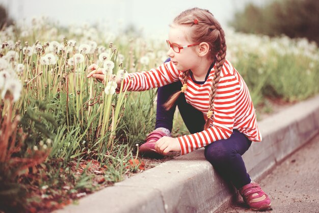 Mooi emotioneel meisje met een bril die met paardebloemen speelt. kindertijd concept