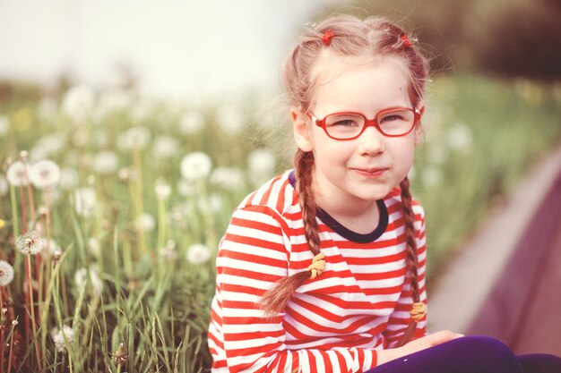 Mooi emotioneel meisje met een bril die met paardebloemen speelt. kindertijd concept