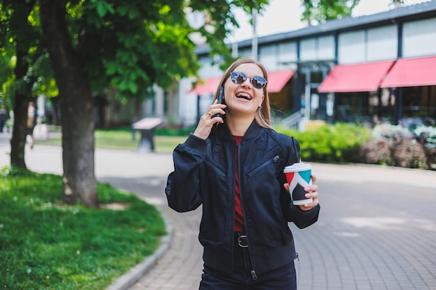 Mooi en jong meisje in zonnebril schrijft een bericht op een mobiele telefoon en buitenshuis koffie drinken