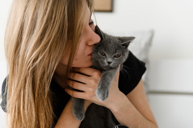 Mooi en sexy meisje liggend op het bed in zelfgemaakte pyjama's met een gelukkig Schots grijs katje in haar armen.