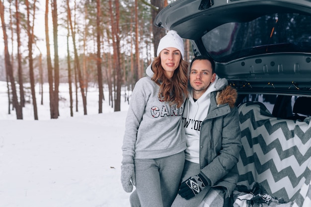 Mooi familiepaar in een sneeuw de winter boszitting in de boomstam van uw auto