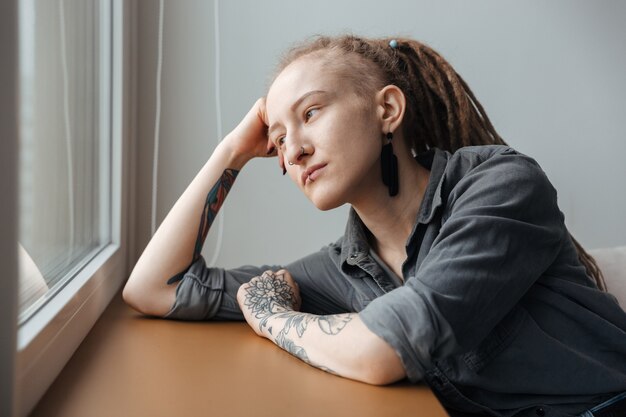 Mooi geconcentreerd jong meisje met dreadlocks binnenshuis poseren kijken naar raam.