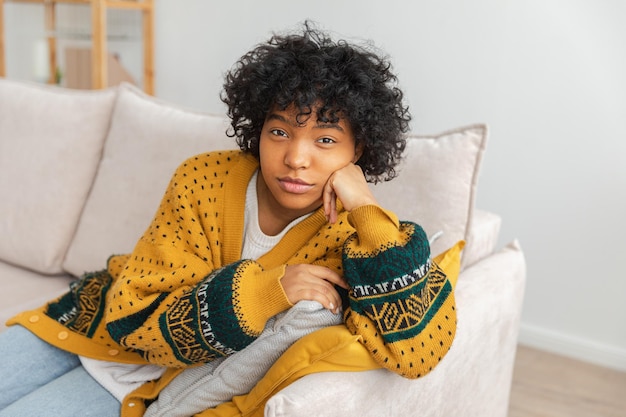 Mooi gelukkig afrikaans amerikaans meisje met een afro-kapsel glimlachend zittend op de bank thuis binnen jou