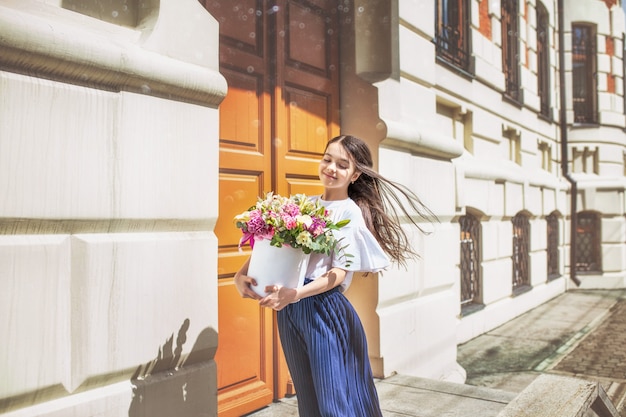 Mooi gelukkig babymeisje dat met boeketten bloemen door de stad loopt