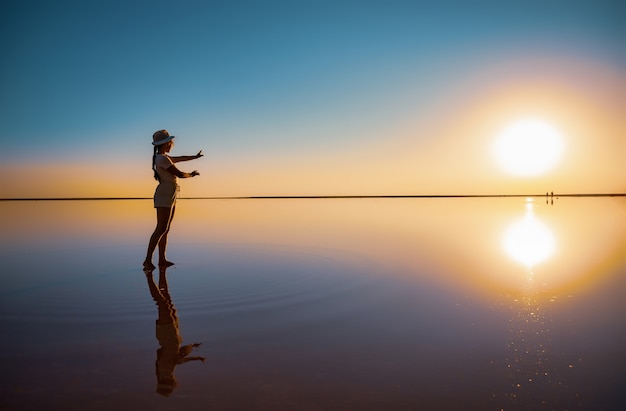 Mooi gelukkig jong meisje wandelingen en poses in een magische pose langs het roze zoutmeer spiegel genietend van de warme avondzon, kijkend naar de vurige zonsondergang en haar spiegelbeeld