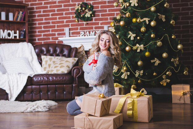 Mooi gelukkig meisje dat een kerstcadeaudoos ontvouwt op een vakantie in de ochtend in een mooie kamerkamer het meisje is open een kerstcadeau in de buurt van de versierde kerstboom concept van wintervakantie