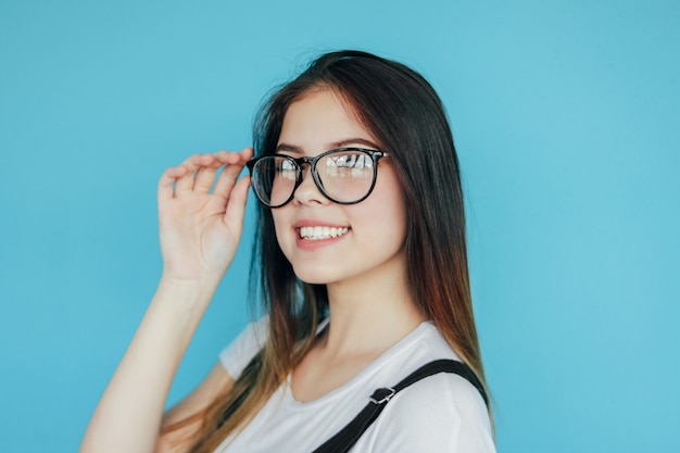 Mooi gelukkig meisje in glazen met donker lang haar in witte die t-shirt op blauw wordt geïsoleerd