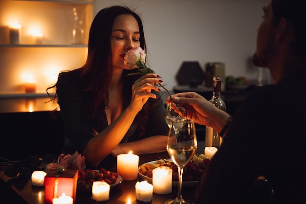 Mooi gepassioneerd paar met een romantisch diner bij kaarslicht thuis, vrouw ruiken een bloem