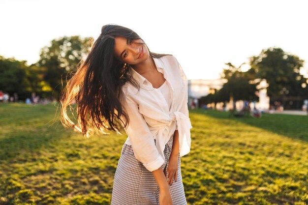 Mooi glimlachend Aziatisch meisje in een wit overhemd dat dromerig in de camera kijkt terwijl ze danst in het stadspark