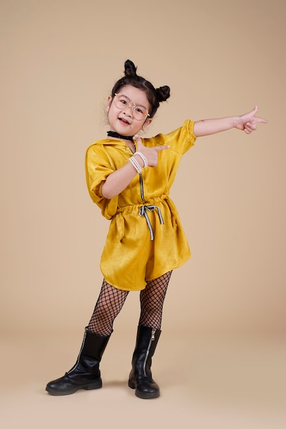 Mooi glimlachend aziatisch mode-meisje in gele jurk op beige achtergrond met vrije tekstruimte