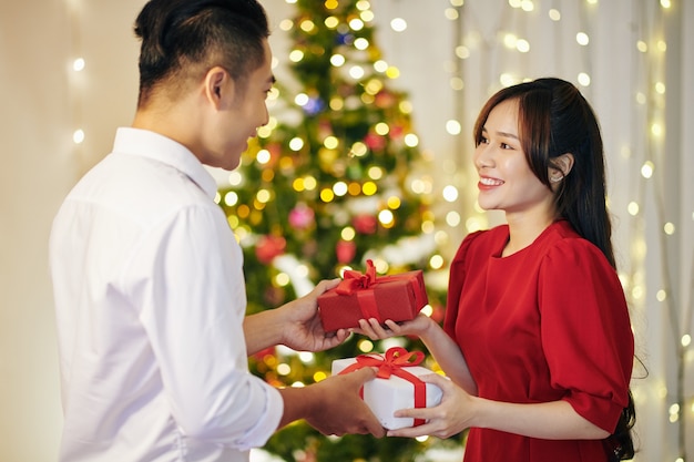 Mooi glimlachend jong vietnamees koppel dat kerstcadeautjes thuis uitwisselt