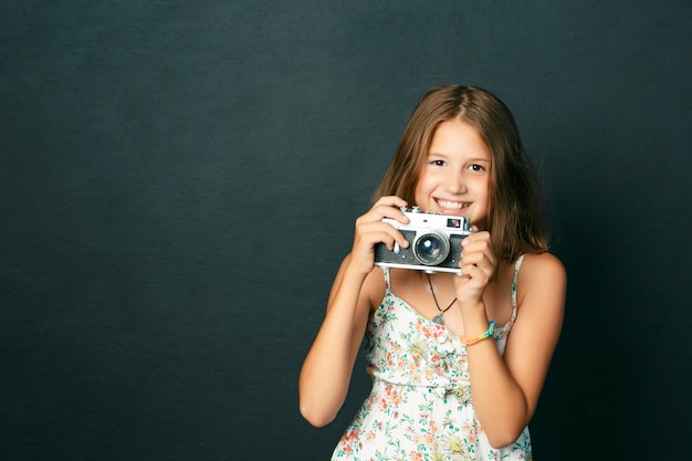 Mooi glimlachend kind (meisje) met witte tanden die een onmiddellijke camera houden