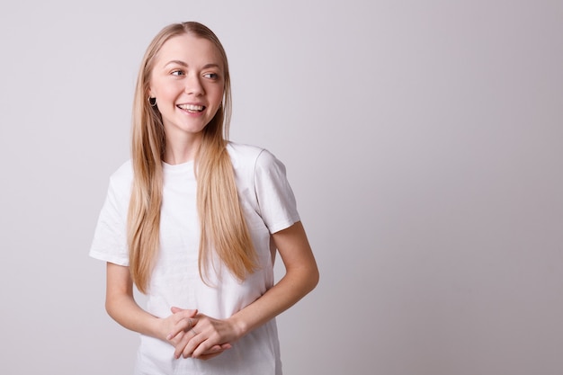 Mooi glimlachend meisje in een wit T-shirt op een witte muur kijkt naar de zijkant