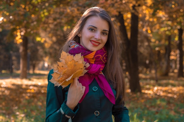 Mooi glimlachend meisje met een roze sjaal die een boeket van bladerenclose-up houdt