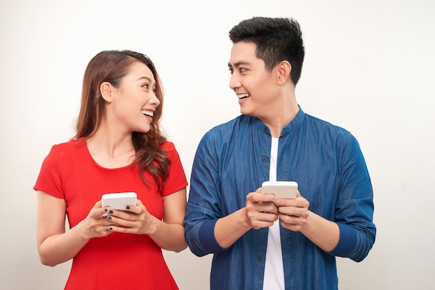 Mooi glimlachend modern paar in vrijetijdskleding met telefoons in handen op een witte muurachtergrond