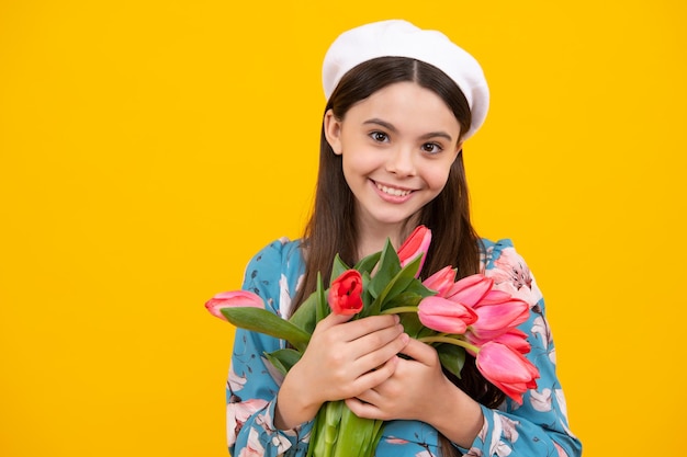 Mooi glimlachend trendy tienermeisje met boeket tulpen op gele studioachtergrond Meisje dat van bloemen geniet