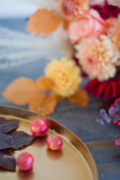 Mooi herfstboeket met oranje en rode bloemen en bessen Herfstboeket en gouden dienblad met kleine appels op een houten tafel