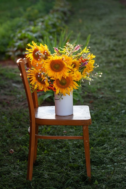 Mooi herfstboeket van felgele zonnebloembloemen in witte vaas op de stoel. Herfst stilleven met tuin bloemen.