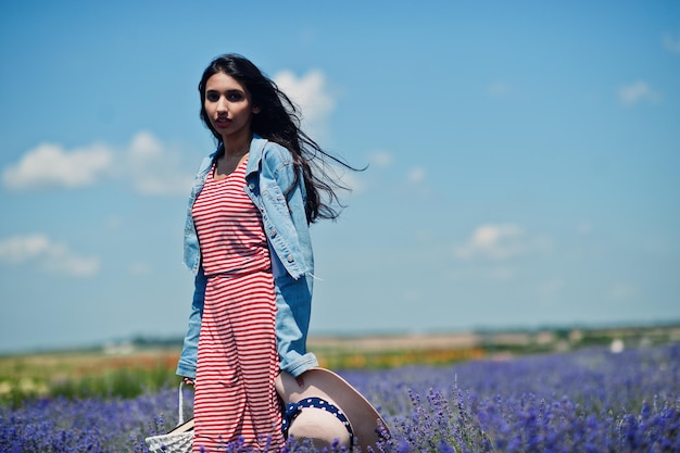 Mooi Indisch meisje in zomerjurk en jeansjasje in paars lavendelveld met mand in de hand en hoed