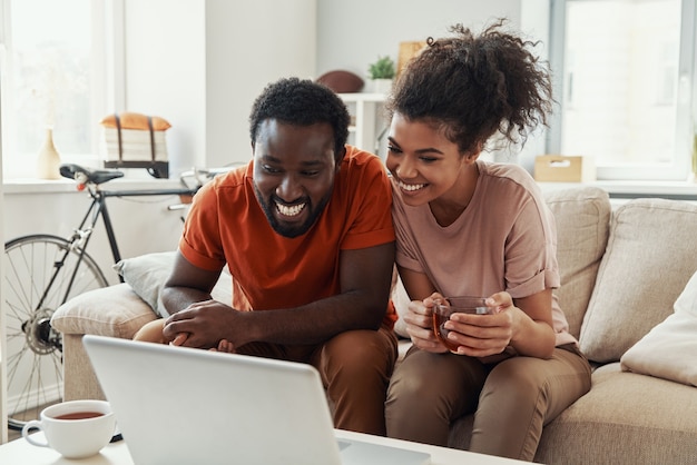 Mooi jong Afrikaans stel dat naar laptop kijkt en glimlacht terwijl ze thuis tijd doorbrengen