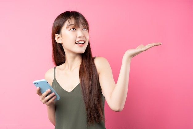 Mooi jong Aziatisch meisje dat telefoon op roze muur gebruikt