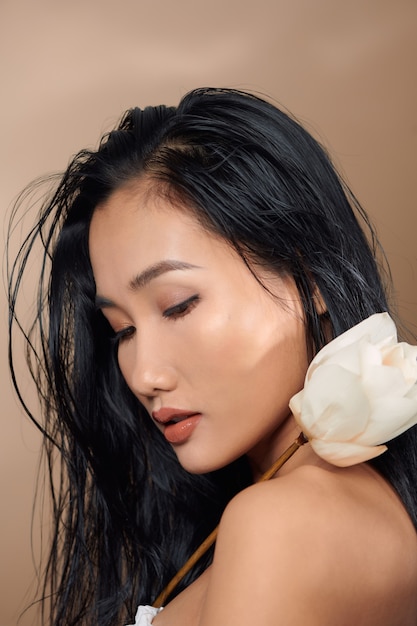 Mooi jong Aziatisch meisje met natuurlijke make-up en nat haar poseren in de studio op een beige achtergrond