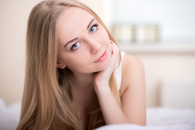 Mooi jong blondemeisje dat op een bed in haar slaapkamer ligt