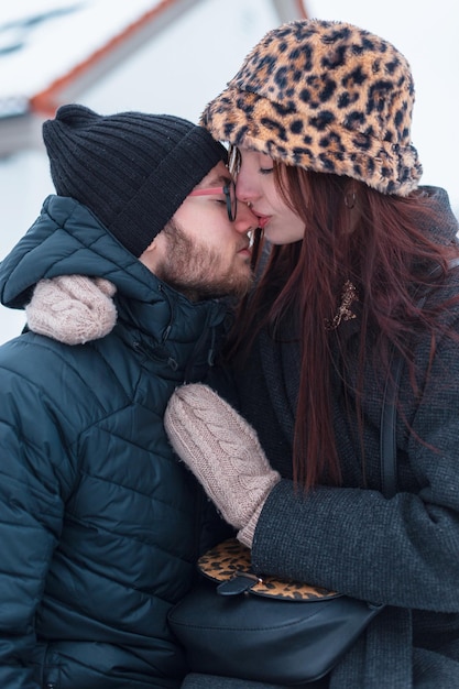 Mooi jong echtpaar in modieuze winterkleding zitten samen en knuffelen in de stad Mooi meisje kust haar vriend op de neus