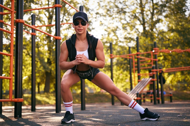 Mooi jong fitness meisje warmt op in het stadion voor de training Aantrekkelijke slanke brunette in een tracksuit zwarte pet en zonnebril Actieve levensstijl