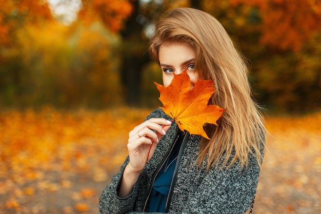 Mooi jong gelukkig meisje met een fel rood-geel herfstblad in het park