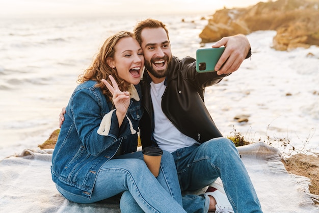 mooi jong kaukasisch stel dat selfie-foto maakt op mobiele telefoon tijdens een wandeling langs de kust