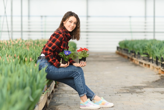 Mooi jong lachend meisje, werknemer met bloemen in kas.