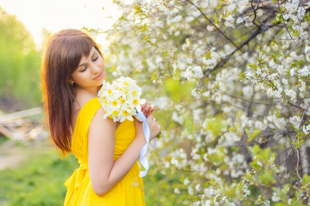 Mooi jong meisje dat met een boeket van bloemen in openlucht in de lente glimlacht
