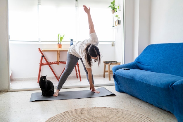 mooi jong meisje dat oefeningen en yoga beoefent in haar woonkamer met een zwarte kat