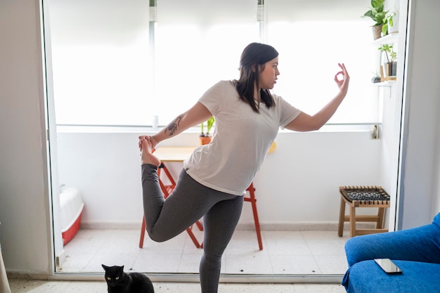 mooi jong meisje dat oefeningen en yoga beoefent in haar woonkamer met een zwarte kat