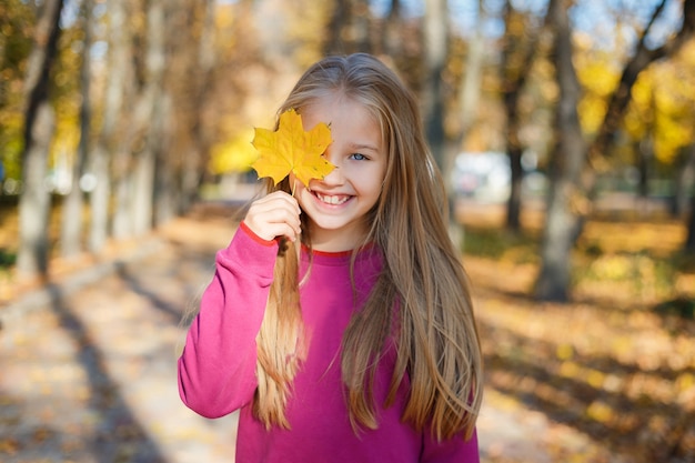 Mooi jong meisje die haar oog behandelen met de herfstblad die van de herfst genieten die zich onder bladeren bevinden. Portret van gelukkig meisje