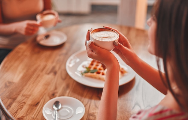 Mooi jong meisje drinkt cappuccino terwijl ze ontspant in een gezellig café, close-up