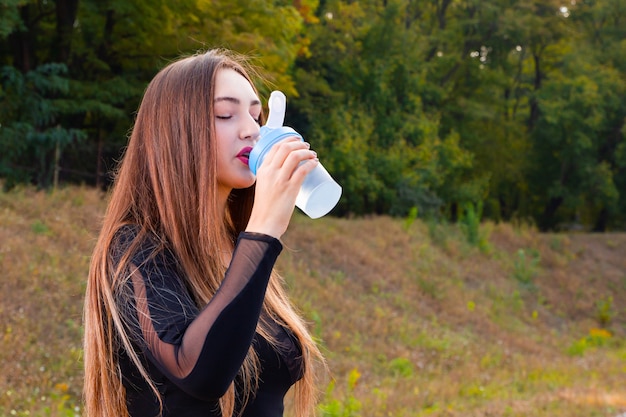 Mooi jong meisje drinkt water in het park na het sporten. Portret van sportieve vrouw drinkwater in park na het joggen. Vrouwelijke atleet na training training. Ruimte kopiëren