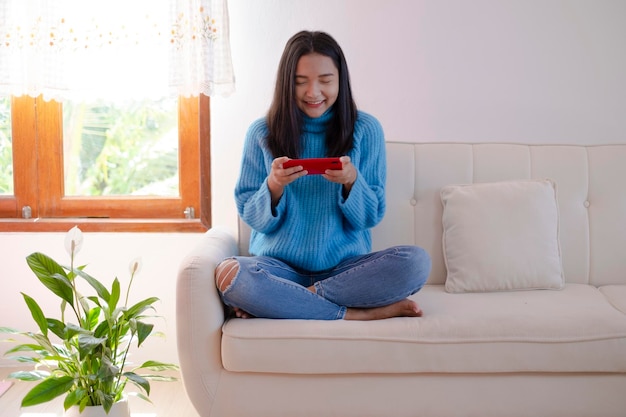 Mooi jong meisje gebruikt smartphone zittend op de bank thuis