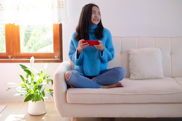 Mooi jong meisje gebruikt smartphone zittend op de bank thuis