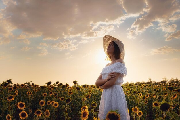 Mooi jong meisje genieten van de natuur op het gebied van zonnebloemen bij zonsondergang