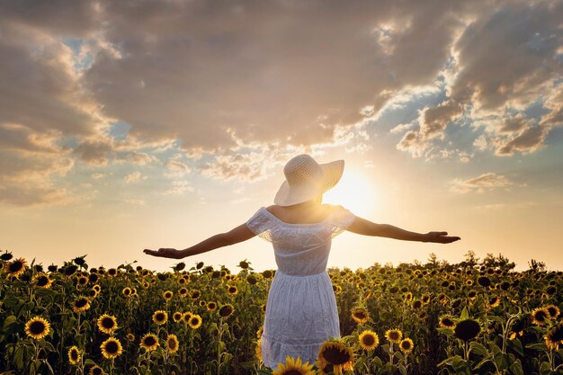 Mooi jong meisje genieten van de natuur op het gebied van zonnebloemen bij zonsondergang