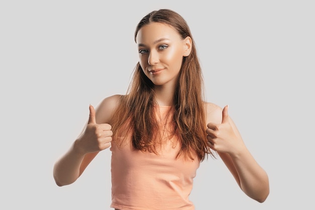 Mooi jong meisje glimlachend en toont duim omhoog gebaar met twee handen op een witte geïsoleerde achtergrond Positieve vrouw wijst naar een idee een plek voor reclame