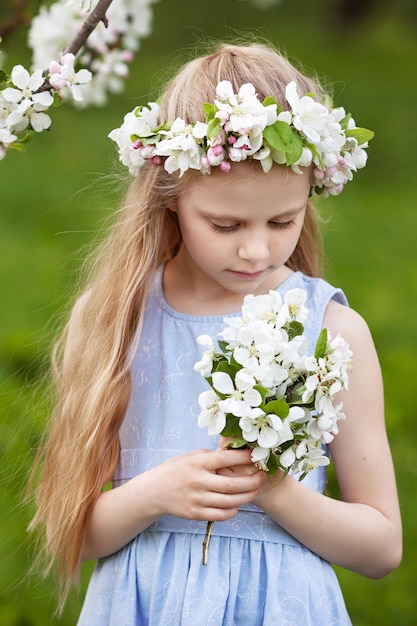 Mooi jong meisje in blauwe jurk in de tuin met bloeiende appelbomen Schattig meisje met een boeket bloemen