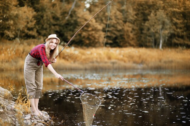 Mooi jong meisje in de herfst bij de rivier met een hengel