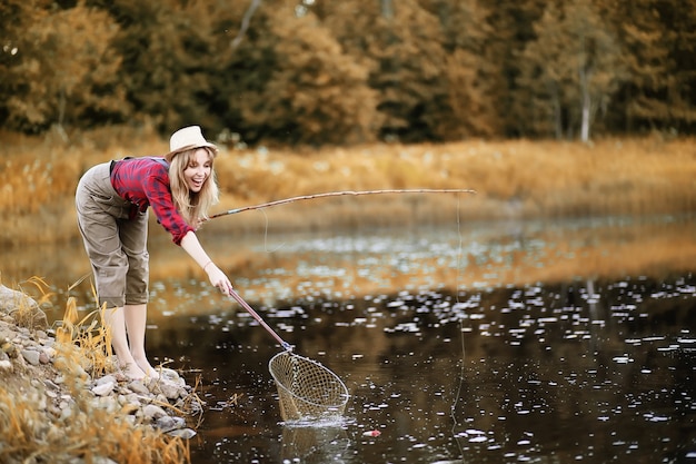 Mooi jong meisje in de herfst bij de rivier met een hengel