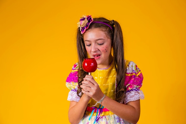 Mooi jong meisje in juni feestkleding die Love Apple Apple-dessert eet bedekt met rode karamel