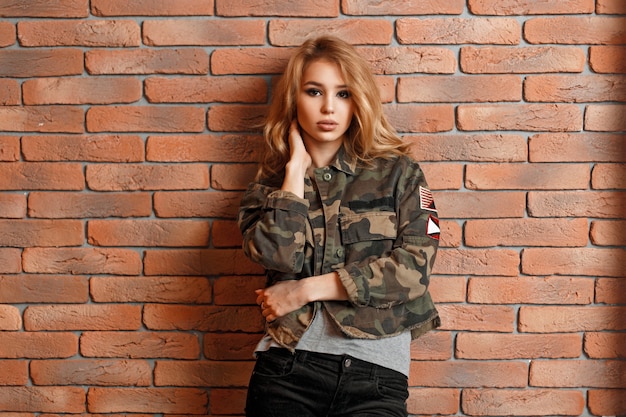 Mooi jong meisje in militair jasje dichtbij rode bakstenen muur