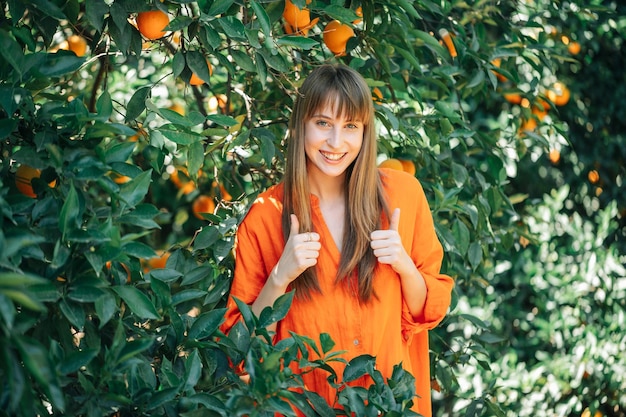 Mooi jong meisje in oranje jurk lacht door perfecte gebaren in oranje tuin te tonen