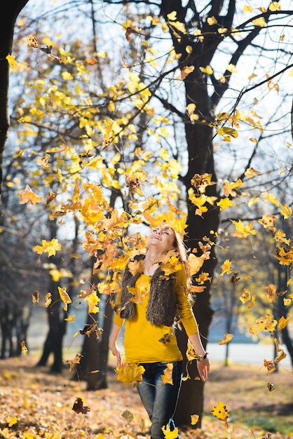 Mooi jong meisje loopt in het herfstpark met gevallen gele bladeren